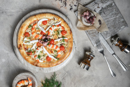 Tasty pizza with  tuna, seafood, shrimps and mini octopus on marble round tray. Garnished on grey stone backdrop with pizza ingredientsの写真素材