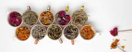 Assortment of dried relaxing tea herbs in colourful cups on white background close up. Calendula, mint, anise hyssop, monarda didyma, wormwood, sage leaves.の写真素材