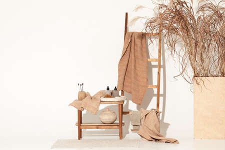 Natural waffle linen towels in earth tones on wood bench and towel ladder with bamboo toothbrushes, rattan baskets, and soap dispenser. Daily body care, spa and wellness zero waste bathroom conceptの写真素材
