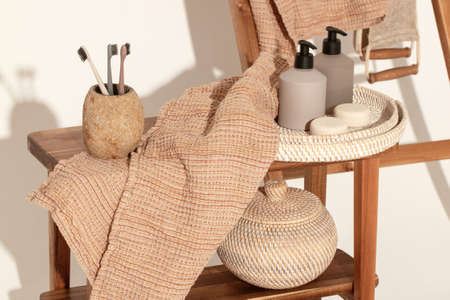 Natural waffle linen towels in earth tones on wood bench and towel ladder with bamboo toothbrushes, rattan baskets, and soap dispenser. Daily body care, spa and wellness zero waste bathroom conceptの写真素材