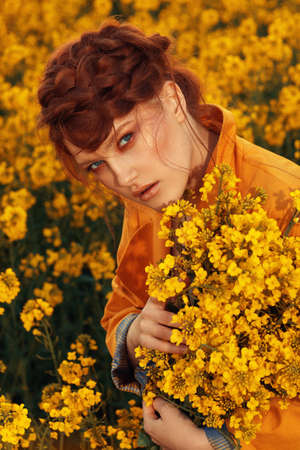 Young fashion model portrait with ginger hair and blue eyes in yellow rapeseed fieldの写真素材