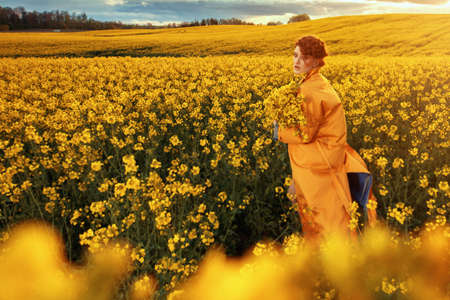 Young fashion model portrait with ginger hair and blue eyes in yellow rapeseed fieldの写真素材