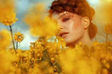 Young fashion model portrait with ginger hair and blue eyes in yellow rapeseed fieldの写真素材