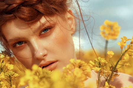 Young fashion model portrait with ginger hair and blue eyes in yellow rapeseed fieldの写真素材