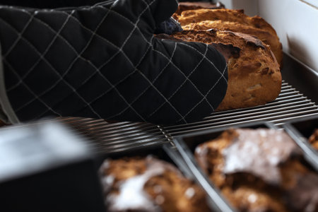 Freshly baked dough bread loafs left to cool down at the bakery. Holding freshly baked hot bread loaf with oven glovesの写真素材