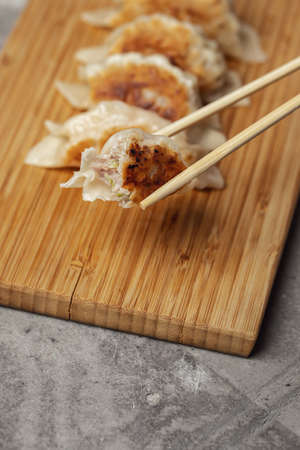 Gyoza or dumplings snack with soy sauce on wood board and grey clay background. Using chopsticksの写真素材