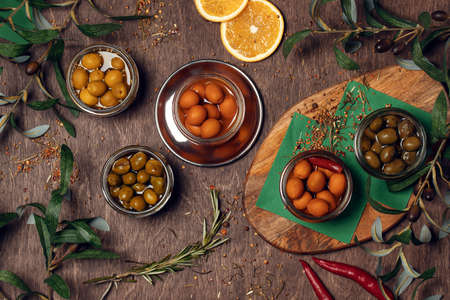 Set of different marinated olives on wood background in bowls decorated with spices and olive leaves.の写真素材