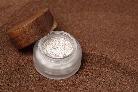 Homemade scrub with brown sugar and coffee in glass jar with wooden lid on brown sand background....