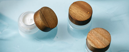 Moisture face cream in glass jar with wood lid on ocean blue wet background. Beauty, spa, wellness zero waste packaging conceptの写真素材