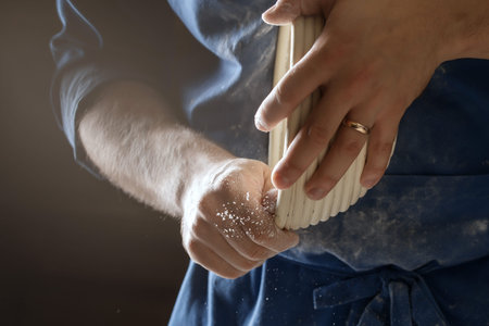 Male baker lightly flouring proofing basket for home made sourdough bread.