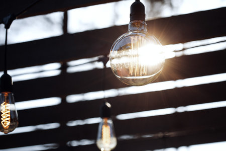 Row of hanging summer terrace lights, small outdoor light bulbs. Lighting bulb in orange warm light...