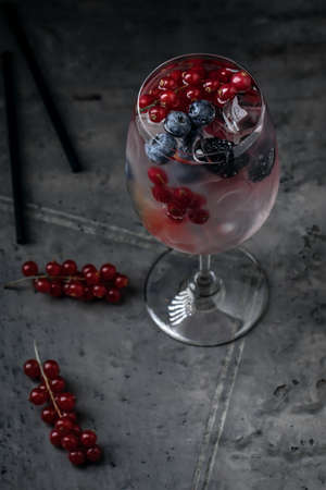 Fresh summer berries cocktail drink in wine glass with red currants and blueberries on grey clay textured backgroundの写真素材