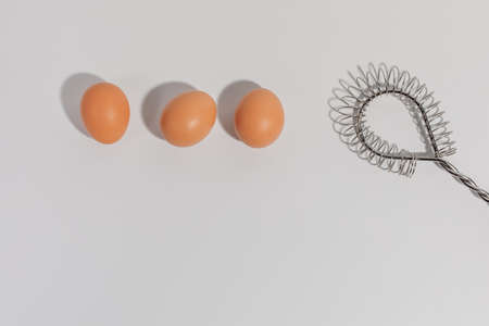 Three eggs and stainless steel Wire Whisk on white backgroundの写真素材