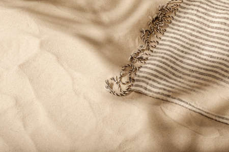 Striped linen beach towel with fringes on sandy beach with shadows from palm tree. Relaxation and tropical summer holidays conceptの写真素材