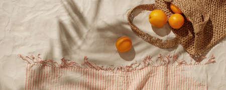 Fresh oranges falling out from woven bag on sandy beach. Linen beach towel with fringes detail. Tropical holidays conceptの写真素材