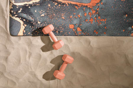 Unrolled grey yoga mat, orange dumbbells on sandy beach. Relaxation and meditation wellbeing. Mindful living conceptの写真素材