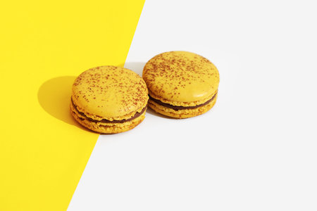 Two Yellow french macaroons on bright yellow and white background.  Delicious meringue cookies. Food...