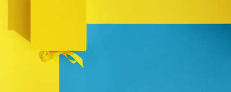 Bright yellow gift box with ribbon bow on yellow and blue  background top view copy space. Birthday present, March 8, Mothers Day, Valentines Day, Easter or spring concept.の写真素材