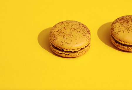 Two Yellow french macaroons on bright yellow background.  Delicious meringue cookies. Food concept