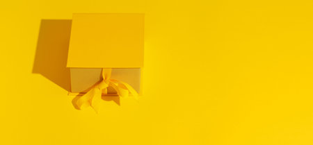 Bright yellow gift box with ribbon bow on yellow background top view copy space