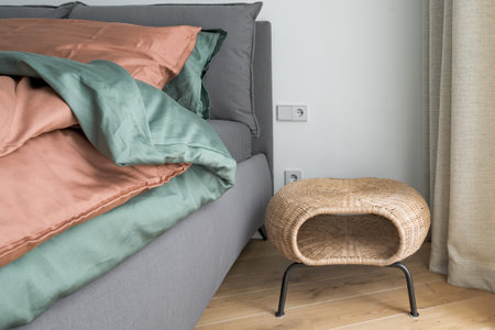 Bedroom interior with rust color linen and cushions on a bed, grey blanket, rattan bedside table and metal wall light.の写真素材