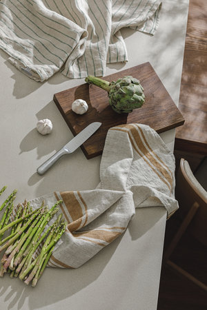 Garlic, asparagus and artichoke on wooden board, linen towels and stainless still kitchen accessories. Healthy food cooking ingredients background with fresh vegetablesの写真素材
