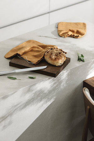 Freshly baked bread on a wooden board, stainless steel bread knife on grey kitchen islandの写真素材