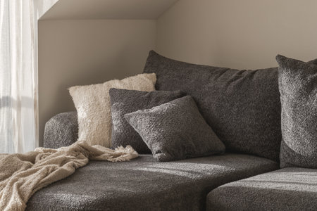 White and grey textured decorative pillows, cozy knitted blanket on a 
dark grey sofa. Wabi-sabi interior details for decorationの写真素材