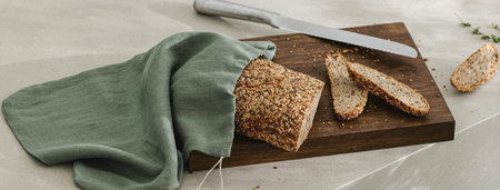 Sliced bread on wooden board in linen bag, fresh herbs and stainless still kitchen knife. Kitchen...