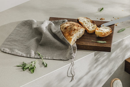 Sliced bread in linen bag on wooden board, fresh herbs and stainless still kitchen knife. Kitchen...