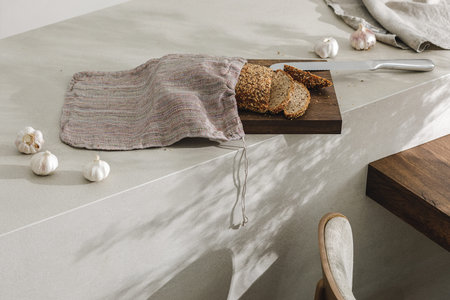 Sliced bread in linen bag on wooden board, garlic and stainless still kitchen knife. Kitchen...