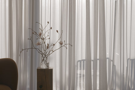 A magnolia branch in a clear glass vase rests on an oak stump, embodying spring in a Japandi interior. The soft blooms and warm wood create a serene, minimalist atmosphere.の写真素材