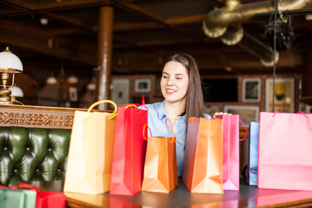 Gorgeous brunette woman sitting in a bistro with a lot of colored gift bagsの写真素材