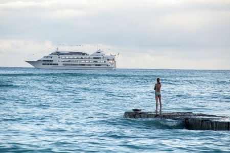 Surfer girl at sunset watches as a large cruise ship passes Waikiki beach in Oahu, Hawaii.のeditorial素材