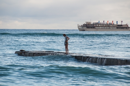 Surfer girl at sunset watches as a large cruise ship passes Waikiki beach in Oahu, Hawaii.のeditorial素材
