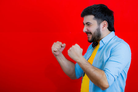 Joyful happy guy in a yellow T-shirt and blue shirt stands on a red background