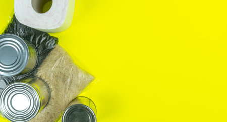 Flatlay Paper bag with food supplies. Quarantine food crisis. Isolation on yellow. Rice, tea,...