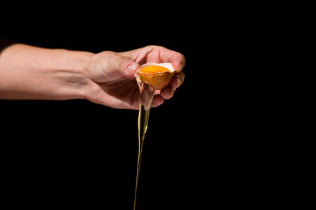 hand holding half egg with yolk and white falling to infinity, with black background, food concept, proteinsの写真素材