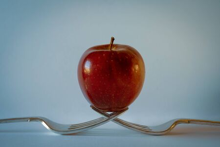 Red apple on two forks with light blue backgroundの写真素材