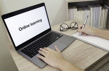 Online learning during coronavirus infection crisis. Cropped photo of hand taking note and using laptop. Concept of self quarantine and work from home. Selective focusの写真素材