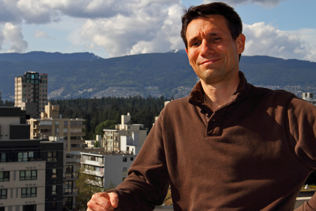 White man smiling, looking at camera. Male Caucasian adult with a satisfied look with brown hair and brown eyes, wearing a brown sweater. Chest and head photograph of a Man standing in front of city and green hills. の写真素材