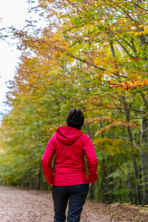 young woman walking happily among beech trees in autumn in red sports and trekking clothes
