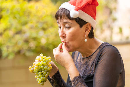 happy woman enjoys a bunch of white grapes at Christmas and wears a Santa Claus hatの写真素材