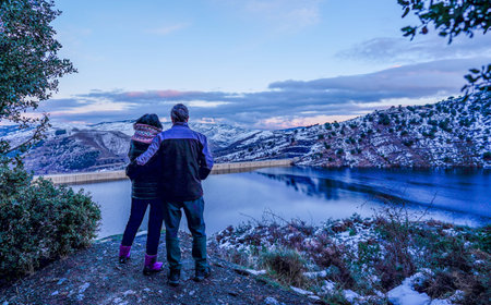Couple enjoying a sunset next to a lake with snow-capped mountainsの写真素材