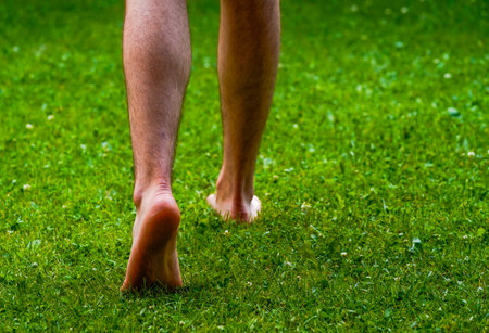 Barefoot man stepping on the summer grass, walking barefoot on the grass, healthy and relaxing.の写真素材