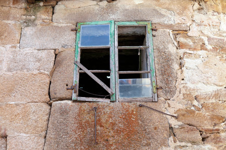 old green window with six holes and two panes in a granite stone wall with lichens and moss, placed...