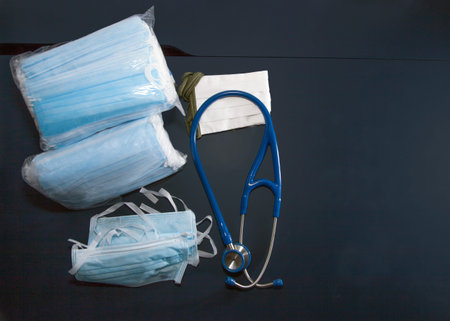 packs of blue surgical masks and stethoscope on dark blue table