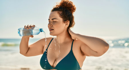 young woman in swimsuit drinking water from bottle on seashoreの素材