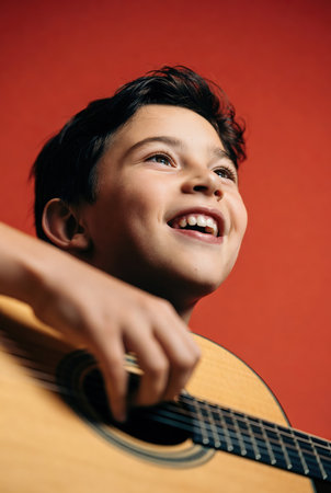 Boy playing guitar, smiling, close-up, isolated on red backgroundの素材