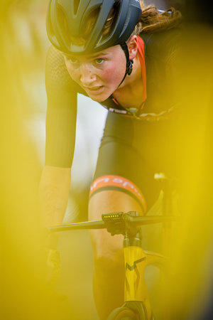 Focused female cyclist in helmet racing on road bike, shot through yellow foreground creating dynamic sports image.の素材